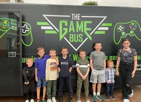 A group of children at a birthday party standing in front of the Game Bus